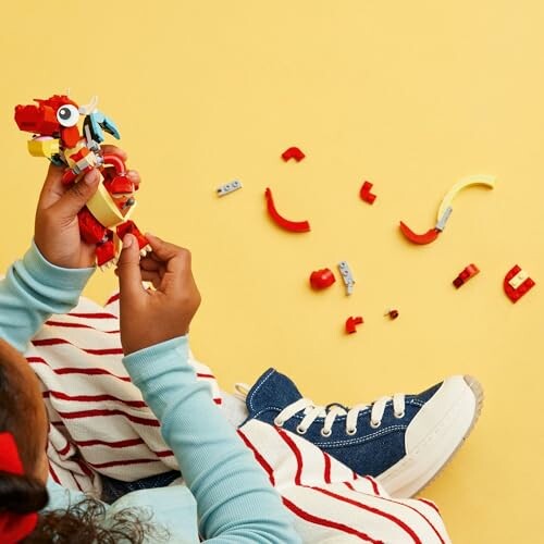 Child assembling a colorful dragon toy on a yellow background.