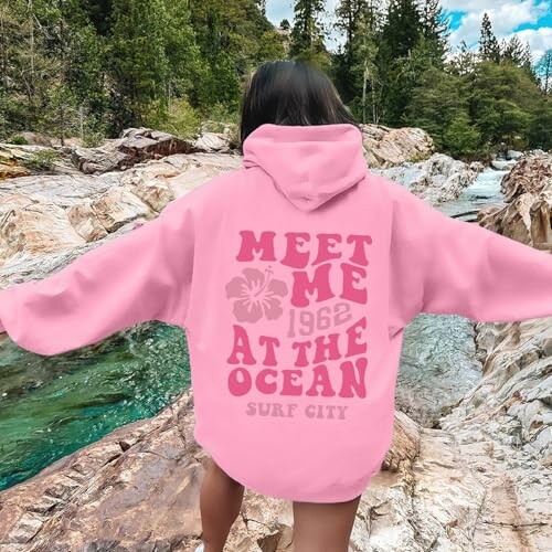 Person in pink hoodie with 'Meet Me at the Ocean' text by a river.